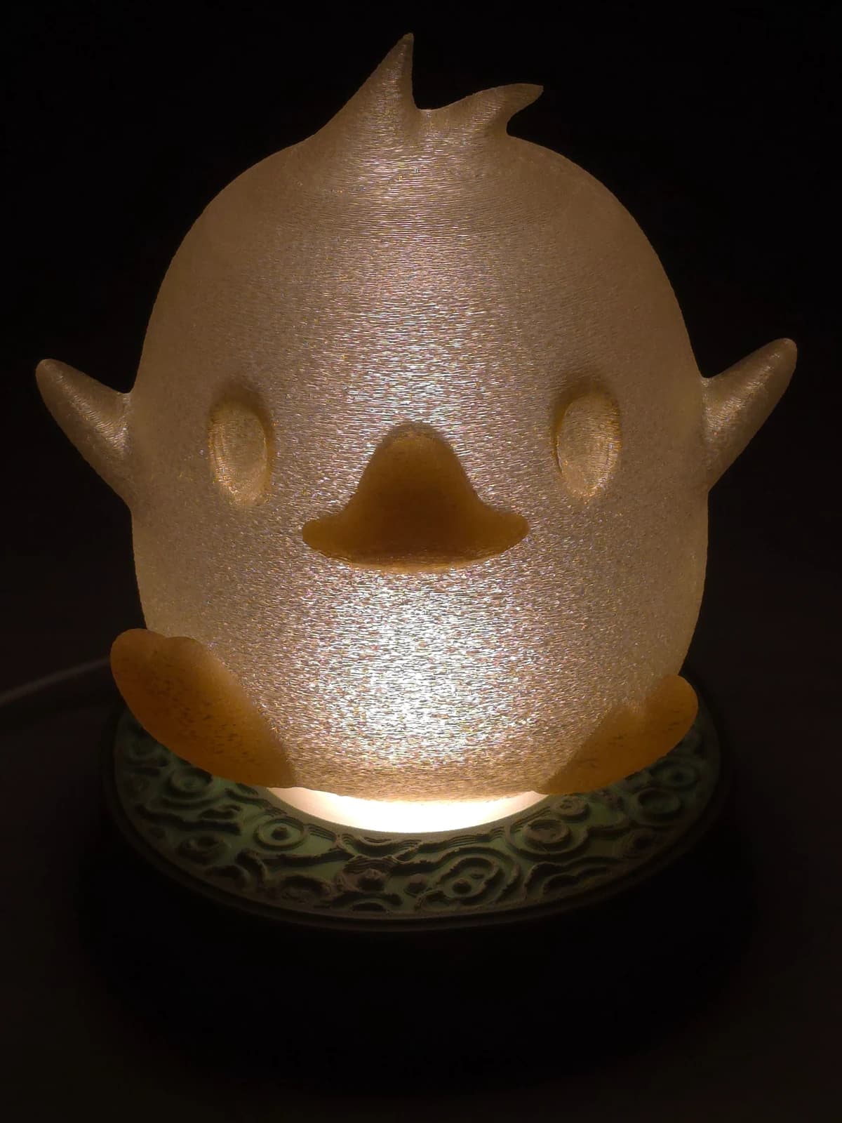 The same chick switched on in the dark — the shade glowing warm yellow